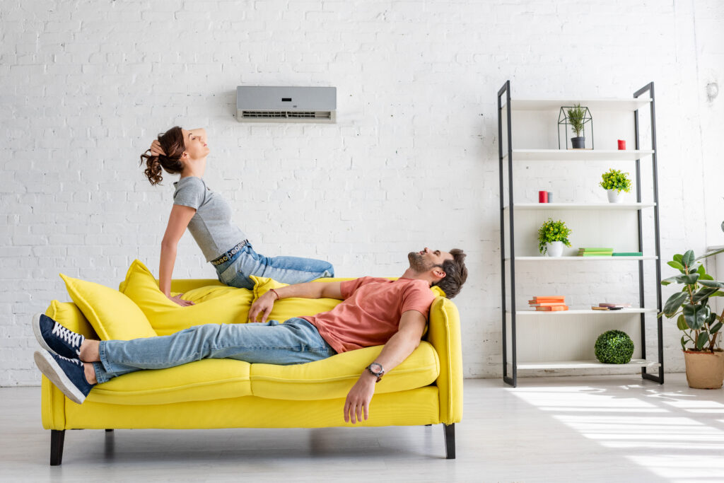 jeune homme et femme se reposant sur un canapé jaune sous le climatiseur à la maison